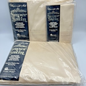 May include: Three packages of Whisper Soft Mills Super Satin sheets and pillowcases. The packages are cream-colored and wrapped in clear plastic. The packaging features dark blue labels with white text that reads "Seamless Woven Fabric Luxurious Satin Sheets" and "Machine Wash & Dry No Ironing."