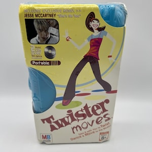 May include: A boxed Twister Moves game. The packaging is yellow and blue, featuring a cartoon illustration of a dancing figure. The box includes text that reads "Twister moves" and "Jesse McCartney 'She's No You'".