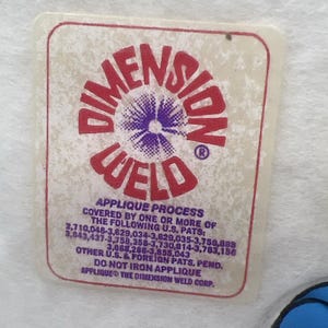 Pu&ograve; includere: Un'etichetta rettangolare con le parole "DIMENSION WELD" in rosso, con un disegno floreale viola e bianco al centro. L'etichetta include anche testo sul processo di applicazione e numeri di brevetto.