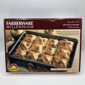 May include: A black rectangular baking pan with a non-stick surface. The pan is 12 1/2 inches by 8 1/2 inches by 1 1/2 inches. The pan is filled with baked goods, such as apple turnovers, and topped with pecans. The pan is part of the Farberware Millennium range of cookware. The box also includes a lifetime limited warranty.