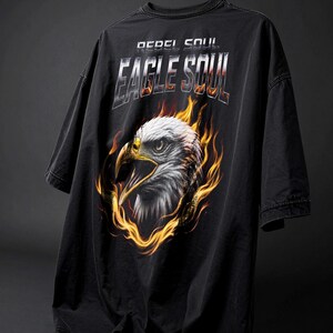 May include: Black oversized t-shirt with the text "REBEL SOUL" and "EAGLE SOUL" in a metallic font. The shirt features a detailed graphic of an eagle's head surrounded by flames. The eagle is white and gray with a yellow beak.
