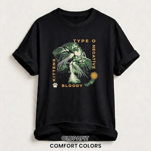 May include: Black t-shirt featuring a green and white illustration of two cats with the text "TYPE O NEGATIVE" and "KITTENS BLOODY". A paw print and sun graphic are also included. The shirt is labeled "COMFORT COLORS" and "OLDPAPIT".