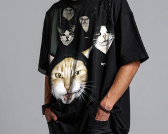 Op de afbeelding: Zwart t-shirt met een grafische print van meerdere katten met verschillende uitdrukkingen. De katten zijn realistisch weergegeven, met gedetailleerde vacht en gezichtskenmerken. Het t-shirt heeft een ronde hals en korte mouwen.