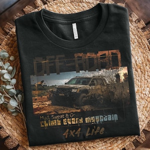 May include: Black t-shirt featuring an off-road vehicle graphic. The design includes the words "OFF-ROAD", "Mud, Sweat & Gears", "Climb every mountain", and "4x4 Life". The image shows a vehicle driving through mud.