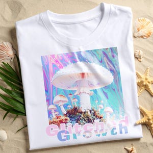 May include: White t-shirt featuring a colorful mushroom graphic with the text "Glitch Growth". The design includes a large white mushroom with smaller mushrooms and a psychedelic background. The shirt is displayed on a sandy surface with seashells.