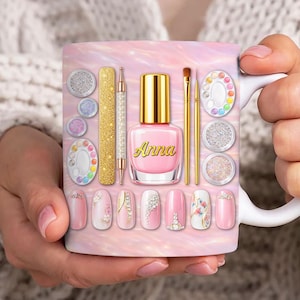 Pode incluir: Uma caneca de cerâmica branca com ferramentas e designs de nail art. A caneca tem um fundo rosa e branco com um frasco de verniz de unhas com o nome "Anna". Designs e ferramentas de nail art, incluindo pincéis e glitter, são exibidos na caneca.