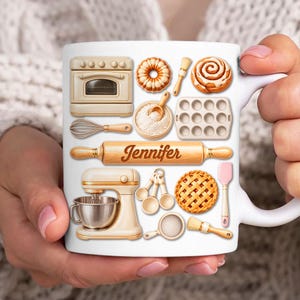 May include: White ceramic mug with baking-themed illustrations, including an oven, mixer, rolling pin with the name "Jennifer", and various baking tools. The mug is held by a person.