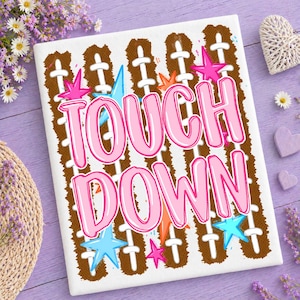 Puede incluir: Un lienzo rectangular con un fondo de patrón de cordones de balón de fútbol americano en color marrón y el texto TOUCH DOWN en letras grandes de color rosa. El diseño está decorado con estrellas dispersas en rosa, naranja y azul claro.