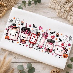 Op de afbeelding: Een wit t-shirt met een rij schattige, antropomorfe medische Halloween-figuren, waaronder een klembord, koffiebeker, bloedzak, injectiespuit, pillenflesje en verpleegsterskap, allemaal versierd met roze strikjes, pompoenen en vleermuizen.