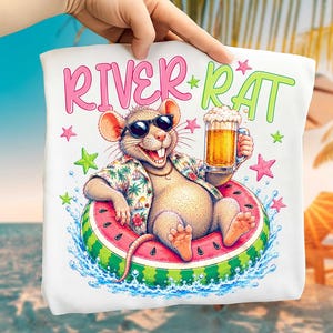 May include: A white t-shirt featuring a graphic of a smiling rat wearing sunglasses and a tropical shirt, floating in a watermelon-patterned inner tube while holding a glass of beer. The text RIVER RAT is printed in pink and green above the rat.