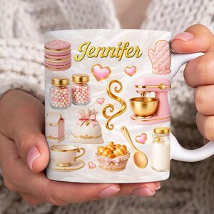 May include: A white ceramic mug with a baking theme, featuring the name "Jennifer" in gold script. The mug is decorated with pink and gold illustrations of baking tools and treats, including a mixer, cookies, and hearts.