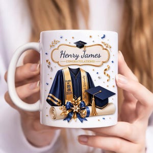 Puede incluir: Taza de cerámica blanca con temática de graduación. El diseño incluye una toga de graduación, birrete, diploma y el texto "Henry James ¡Felicidades!" en una pancarta decorativa. Acentos dorados y azules completan el diseño.