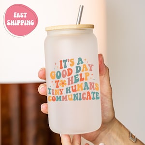 May include: Frosted glass tumbler with a bamboo lid and a silver straw. The tumbler has the text "It's a good day to help tiny humans communicate" in colorful retro lettering. The tumbler is held by a person.
