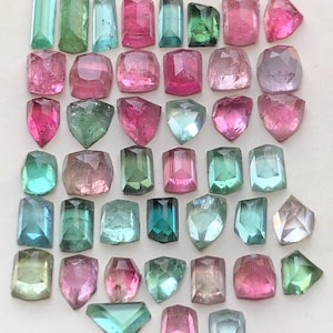 May include: A collection of loose, faceted gemstones in various shapes and sizes, featuring a vibrant colour palette of pink, green, teal, and light blue. These polished, translucent stones are arranged in a grid-like pattern on a plain surface.