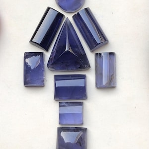 Peut inclure: Un assortiment de pierres précieuses polies, bleu foncé, de formes variées, dont une sphère, un triangle, des rectangles et des carrés. Les pierres sont disposées sur un fond clair, mettant en valeur leurs surfaces réfléchissantes et leur couleur riche.