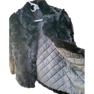 May include: A black fur coat with a quilted lining, hanging on a white hanger. The coat has a collar and is open, revealing the interior lining. The fur appears soft and plush.