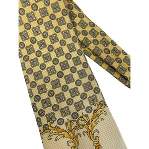 May include: A yellow tie with a repeating geometric pattern in black and white. The tie has a decorative gold and yellow floral design at the bottom. The tie is made of a smooth, possibly silk, material.