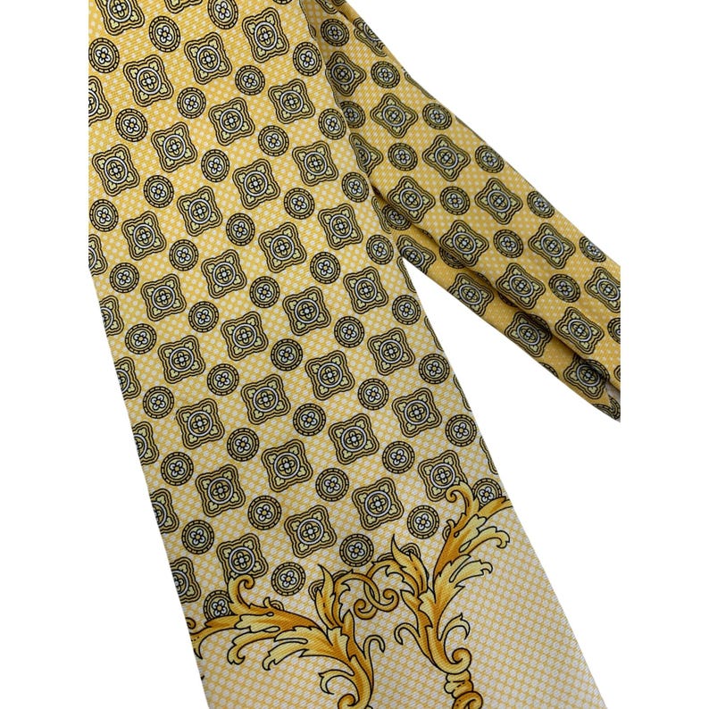 May include: A yellow tie with a repeating geometric pattern in black and white. The tie has a decorative gold and yellow floral design at the bottom. The tie is made of a smooth, possibly silk, material.