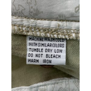 May include: A close-up of a care label with instructions for washing. The label is white with black text that reads: MACHINE WASH COLD WITH SIMILAR COLORS, TUMBLE DRY LOW, DO NOT BLEACH, WARM IRON.