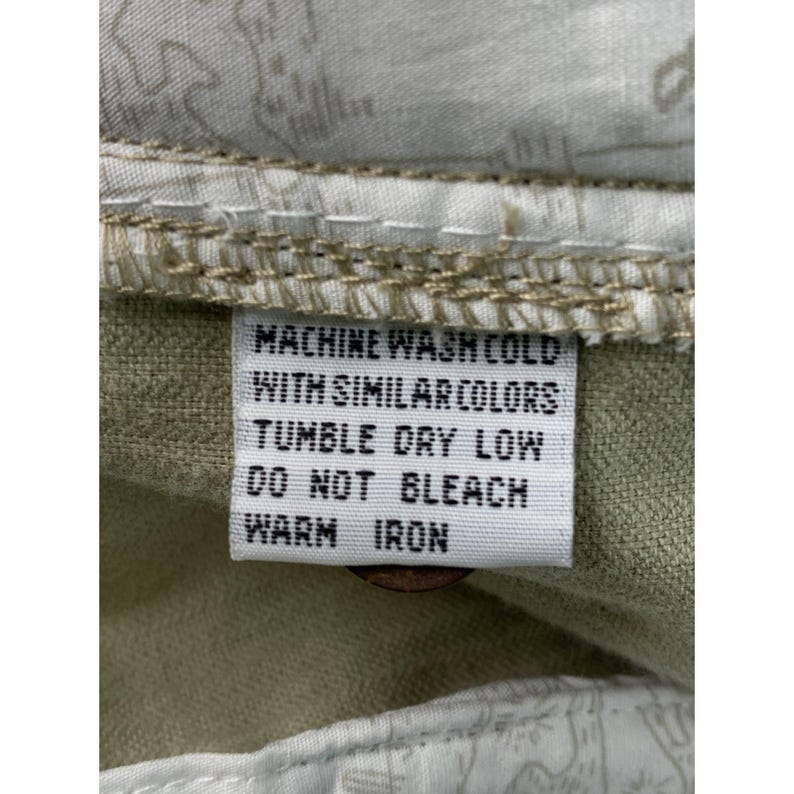 May include: A close-up of a care label with instructions for washing. The label is white with black text that reads: MACHINE WASH COLD WITH SIMILAR COLORS, TUMBLE DRY LOW, DO NOT BLEACH, WARM IRON.