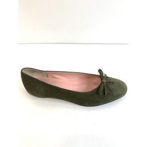 May include: Olive green suede ballet flat with a small bow detail on the toe. The shoe has a rounded toe and a low heel. The interior is a light pink color.