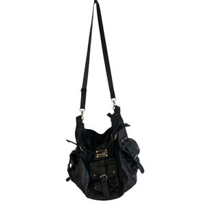May include: Black shoulder bag with multiple pockets and a long adjustable strap. The bag features gold-colored hardware, including buckles and a small rectangular plate. The bag has a slouchy design and is made of a textured material.