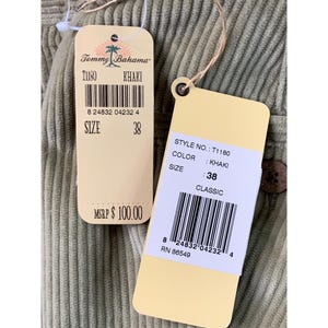 May include: Close-up of khaki-colored corduroy fabric with two attached tags. The tags display the brand "Tommy Bahama", style number T1180, and size 38. The fabric has a ribbed texture.