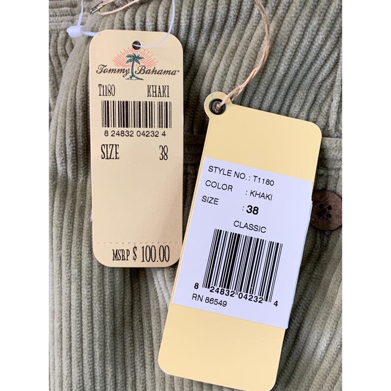 May include: Close-up of khaki-colored corduroy fabric with two attached tags. The tags display the brand "Tommy Bahama", style number T1180, and size 38. The fabric has a ribbed texture.