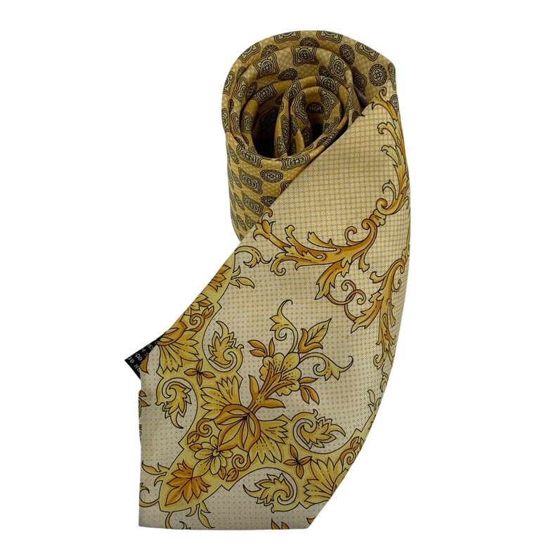 May include: Rolled silk tie with a cream background and gold floral and scrollwork design. The reverse side features a geometric pattern in gold and cream. A small black tag is visible.