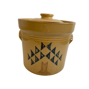 May include: A tan ceramic crock with a lid, featuring a tree design made of blue triangles. The crock has two handles and a rounded shape. The lid has a small knob for easy removal. A vintage kitchenware item.