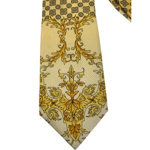 May include: A yellow necktie with a repeating pattern of gold floral and scroll designs. The tie has a pointed end and a small, repeating geometric pattern at the top. The overall design is ornate and detailed.