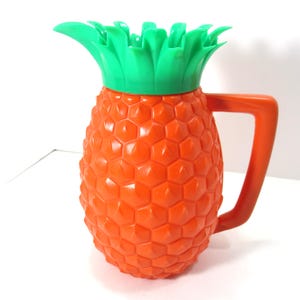 May include: Orange plastic pitcher shaped like a pineapple with green plastic leaves on top.