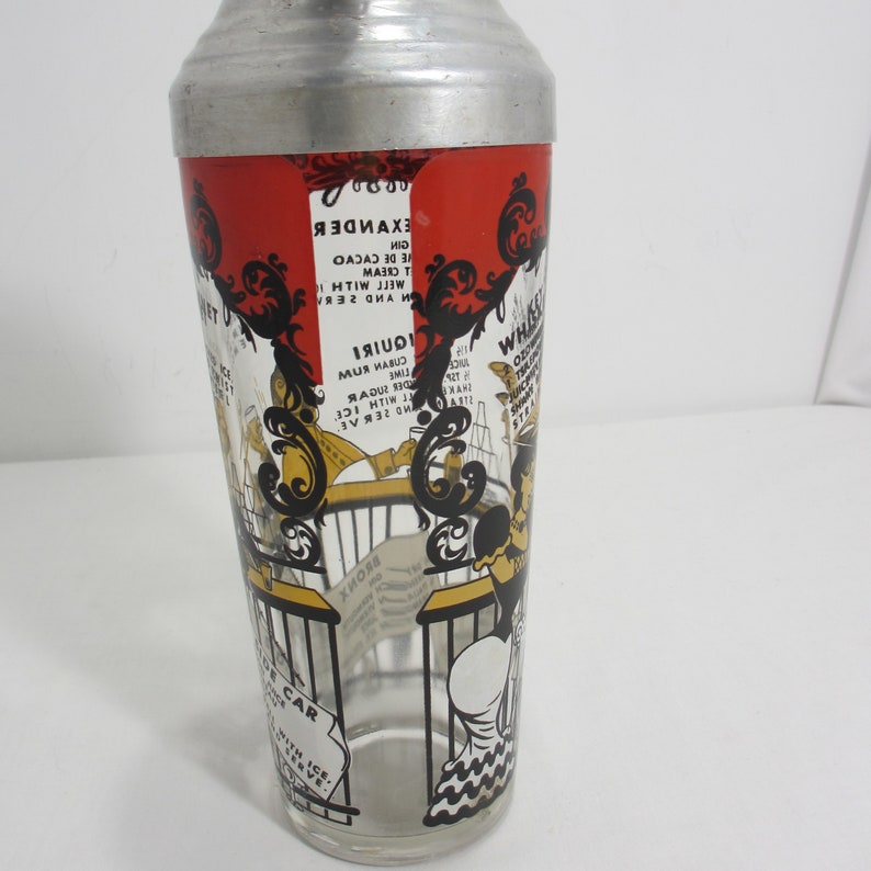 May include: A vintage glass cocktail shaker with a red, black and yellow design. The shaker features a cartoon illustration of a woman holding a glass of liquor. The shaker has a metal top and a glass bottom. The text on the shaker includes cocktail recipes, such as "Alexander", "Whiskey Sour", and "Bronx".