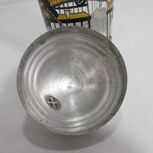 May include: A silver metal shaker lid with a small hole in the centre. The lid has a circular design with concentric circles.