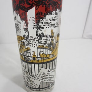 May include: A vintage glass cocktail shaker featuring black and yellow illustrations of people at a bar. The shaker includes recipes for classic cocktails such as Alexander, Daiquiri, Bacardi, and Bronx. The recipes are written in black text on a white background.