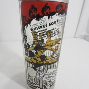 May include: A vintage glass cocktail shaker with a red, black and gold design. The shaker features a recipe for a "Whiskey Sour" with a whimsical illustration of a woman in a hat and a cat.