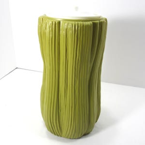 May include: A green plastic container shaped like a tree stump with a white lid.