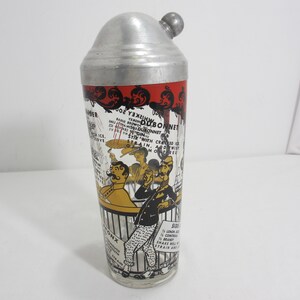 May include: A vintage cocktail shaker with a silver top and a glass bottom. The glass features a colourful illustration of two men in a bar with a recipe for a "Dubonnet" cocktail printed on the side.
