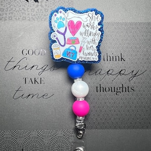 Può includere: Un badge reel a tema veterinario con un design di perline blu, bianche e rosa. Il badge presenta uno stetoscopio, un'impronta di zampa, un cuore e le parole "She works willingly with her hands". Include la parola "VET".