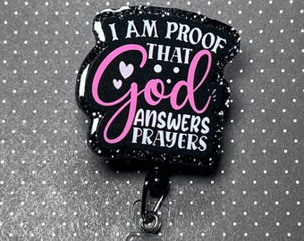 May include: Black badge reel with the text "I AM PROOF THAT God ANSWERS PRAYERS" in white and pink. The badge reel has a glittery border and a clear plastic ID holder with a pink button.