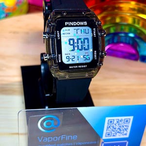 Könnte beinhalten: Eine schwarze Digitaluhr mit transparentem Gehäuse, die die Uhrzeit 9:00 anzeigt. Das Zifferblatt zeigt den Tag als THU und das Datum als 9-21 an. Die Uhr trägt die Aufschrift "PINDOWS" und "WATER RESIST". Die Uhr steht auf einem schwarzen Ständer.