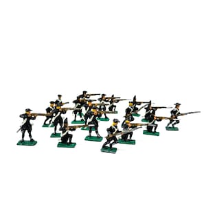 Puede incluir: Un conjunto de soldados de juguete en miniatura con uniformes negros y detalles blancos, sosteniendo rifles. Las figuras están sobre bases verdes, sobre un fondo blanco. Los soldados de juguete están en varias poses, sugiriendo una escena de batalla.