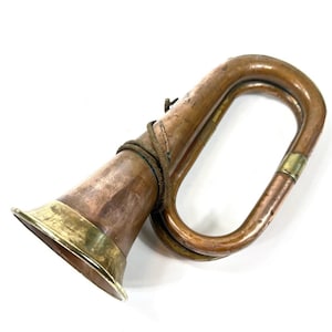 May include: A vintage copper bugle with brass accents. The bugle has a flared bell and a curved body. A rope is wrapped around the body. The instrument is likely used for signaling or ceremonial purposes.