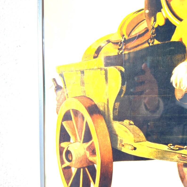 May include: A framed vintage print depicting a yellow and brown beer wagon with a bottle of wine. The wagon has a large wooden wheel and is attached to a chain. The background is a light color.