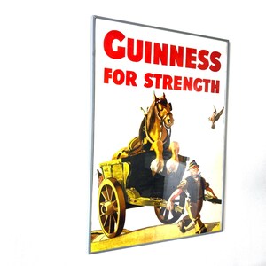 May include: Vintage Guinness advertisement poster. The poster features a brown horse pulling a yellow cart, with a man walking alongside. The text "GUINNESS FOR STRENGTH" is in red letters at the top. A bird is flying in the background.
