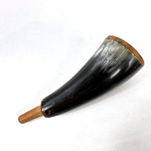 May include: A curved horn with a wooden mouthpiece. The horn's colour graduates from dark black to greyish-white near the opening. The mouthpiece is a light brown colour.