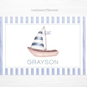 May include: A blue and white striped sailboat with a white flag on a white background with a blue and white striped border. The name Grayson is written below the sailboat.