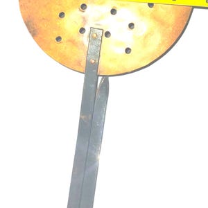 May include: A round, copper-colored kitchen utensil with multiple holes, attached to a dark metal handle. The diameter of the round part is approximately 5 inches. The handle is riveted to the round part.