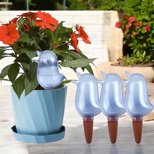 May include: A blue bird-shaped plant waterer is placed in a blue pot with orange flowers. Three additional bird-shaped waterers are displayed next to the pot. The waterers have a brown, cone-shaped base.