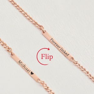 May include: Rose gold chain necklaces with rectangular pendants. One pendant reads "Michael" with a heart symbol, the other reads "Forever linked". The chains and pendants are a warm, metallic color.